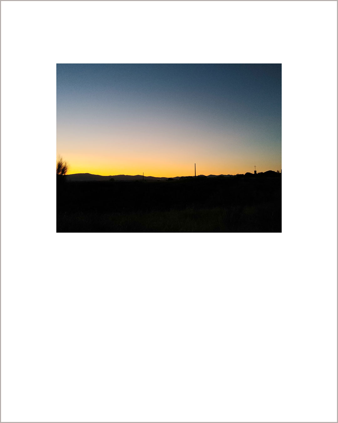 Fotografía horizontal de un atardecer, con el suelo negro y el cielo haciendo un degradado del amarillo al azul plomizo.