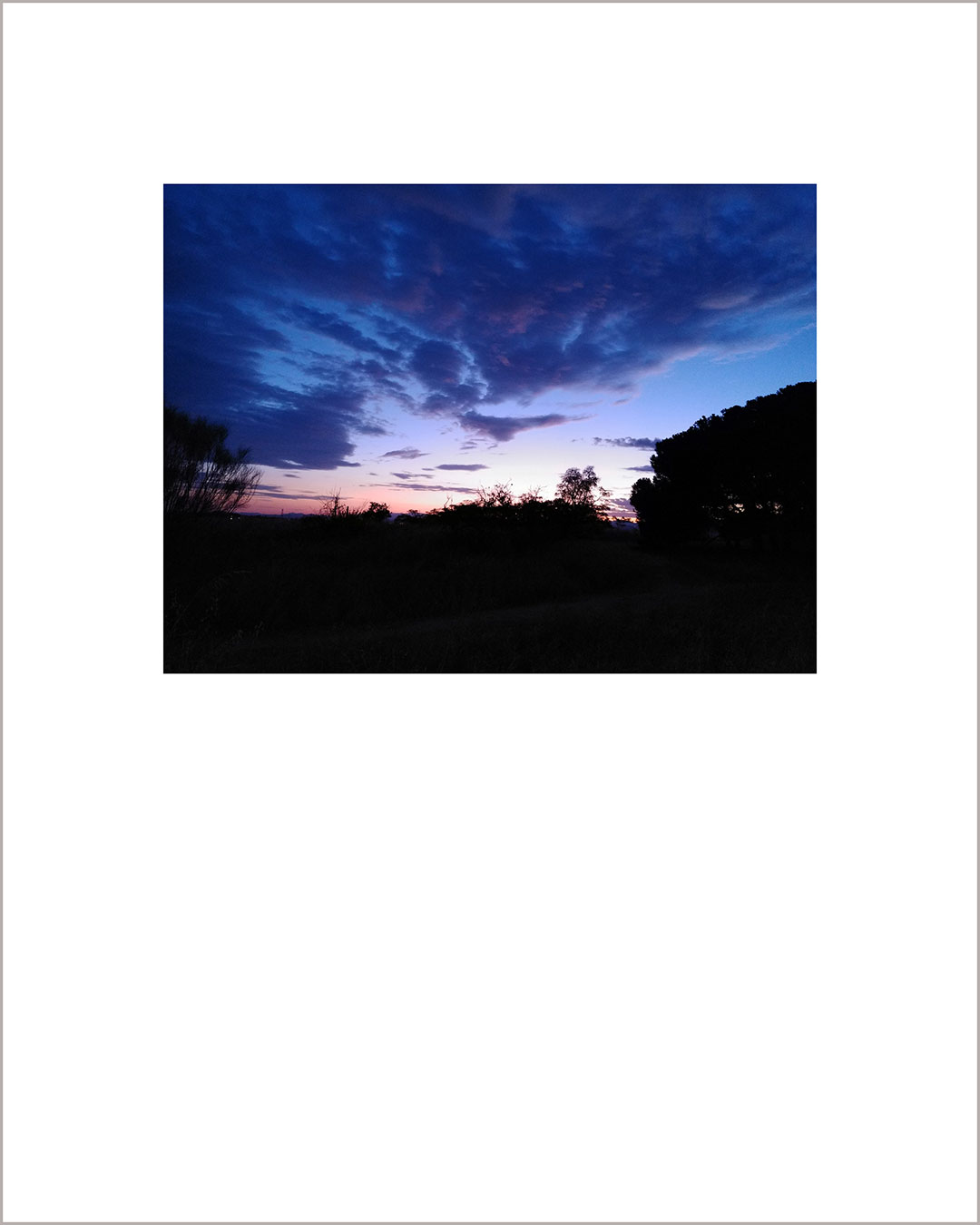 Fotografía horizontal de un atardecer, con el suelo negro y el cielo con grandes nubes de color añil.