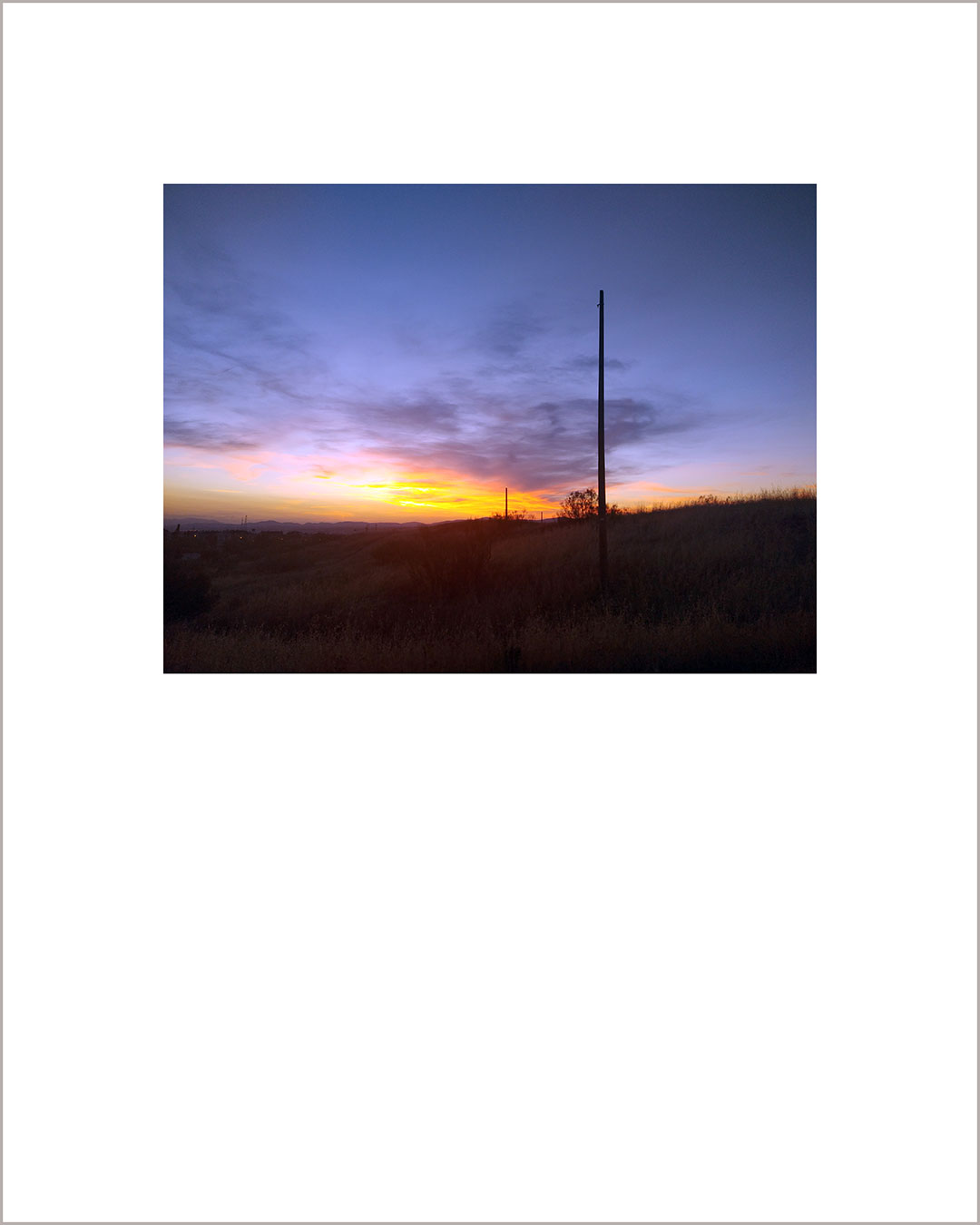 Fotografía horizontal de un atardecer, con el suelo negro y el cielo amarillo y violeta.