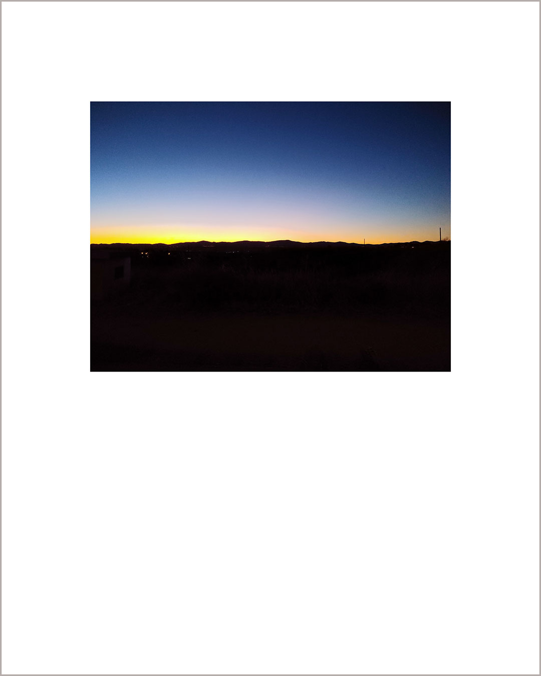 Fotografía horizontal de un atardecer, el suelo es negro y en el horizonte se dibuja una línea amarilla que degrada hacia el cielo añil.