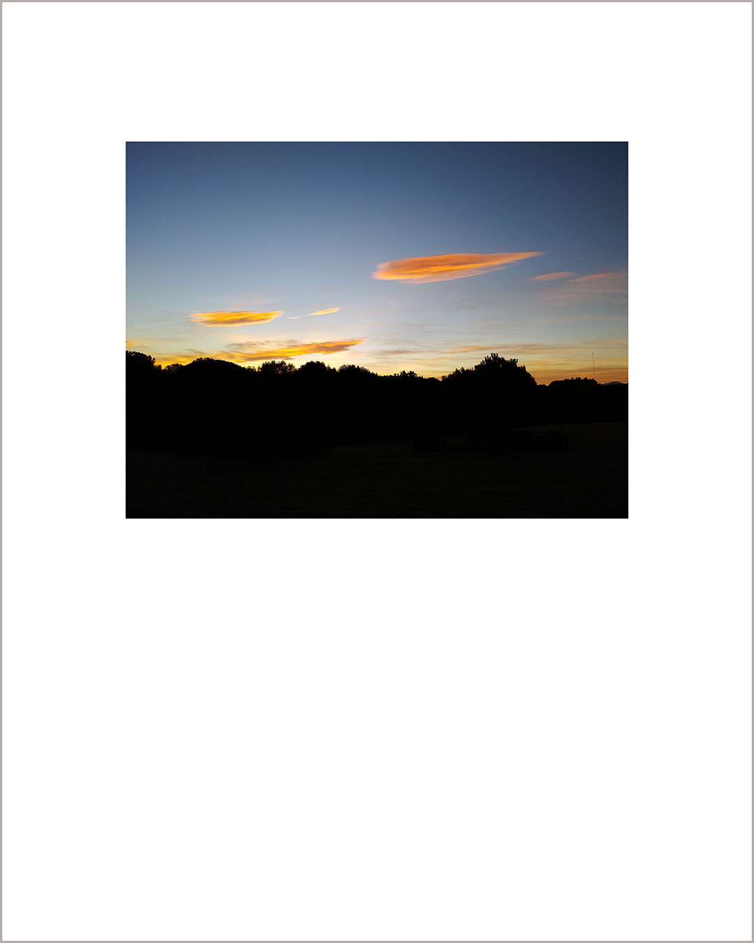 Fotografía horizontal de un atardecer, el suelo es negro y en el cielo azul destacan pequeñas nubes naranjas.