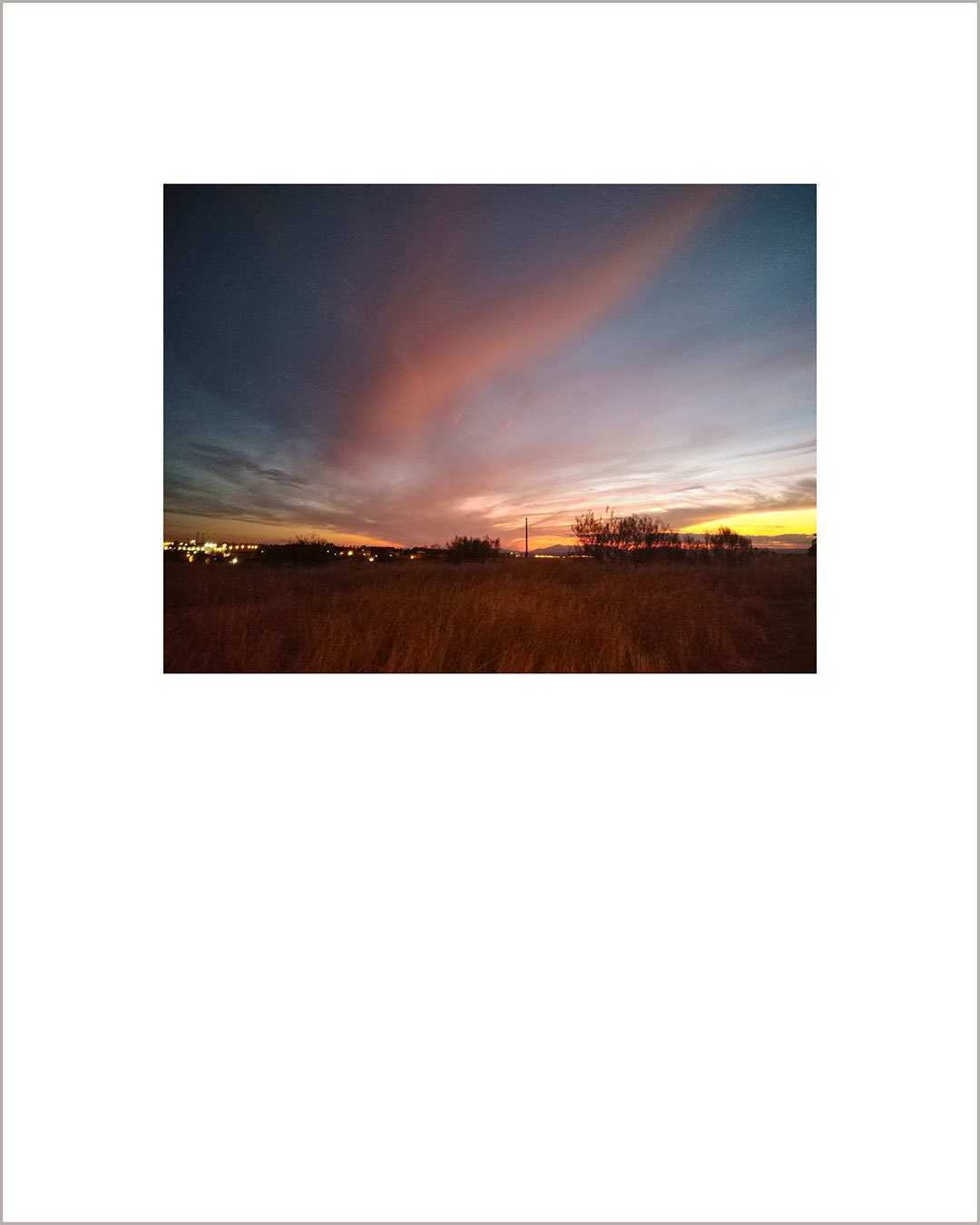 Fotografía horizontal de un atardecer, en el horizonte destacan una luces lejanas, una gran nube rosa de desliza hacia el fondo.