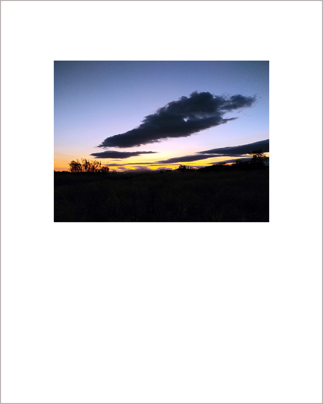 Fotografía horizontal de un atardecer, el suelo es negro y en el cielo añil hay una gran nube oscura.