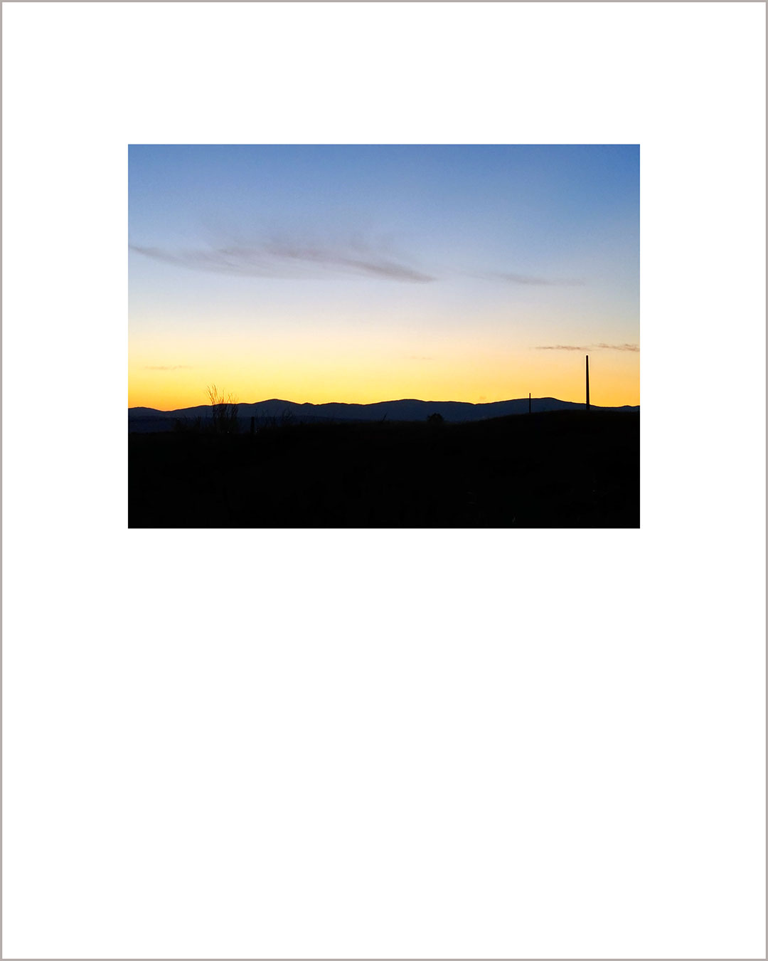 Fotografía horizontal de un atardecer, el suelo es negro, y el cielo hace un degradado del amarillo al azul.