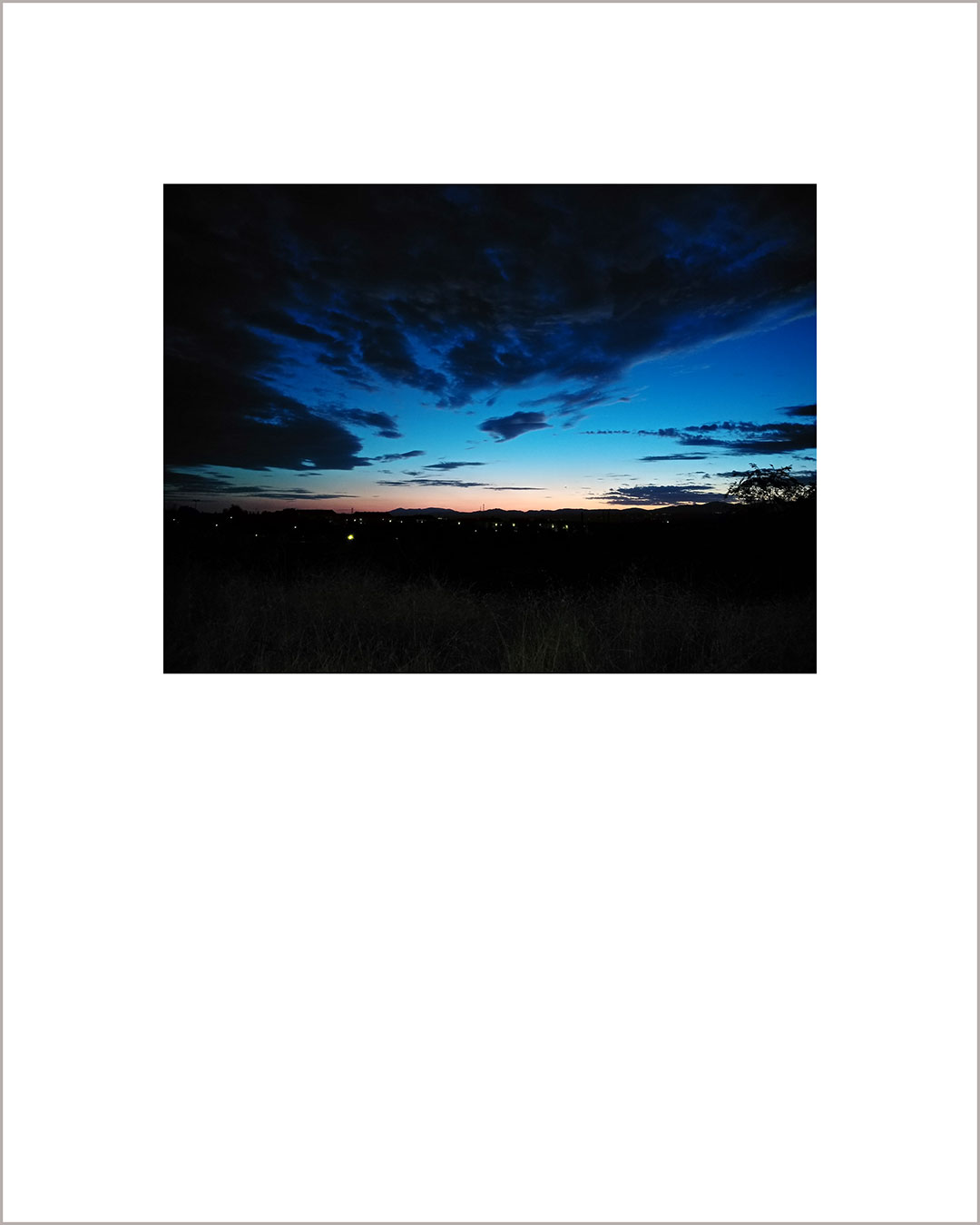 Fotografía horizontal de un anochecer, con suelo negro y cielo añil con grandes nubes negras.