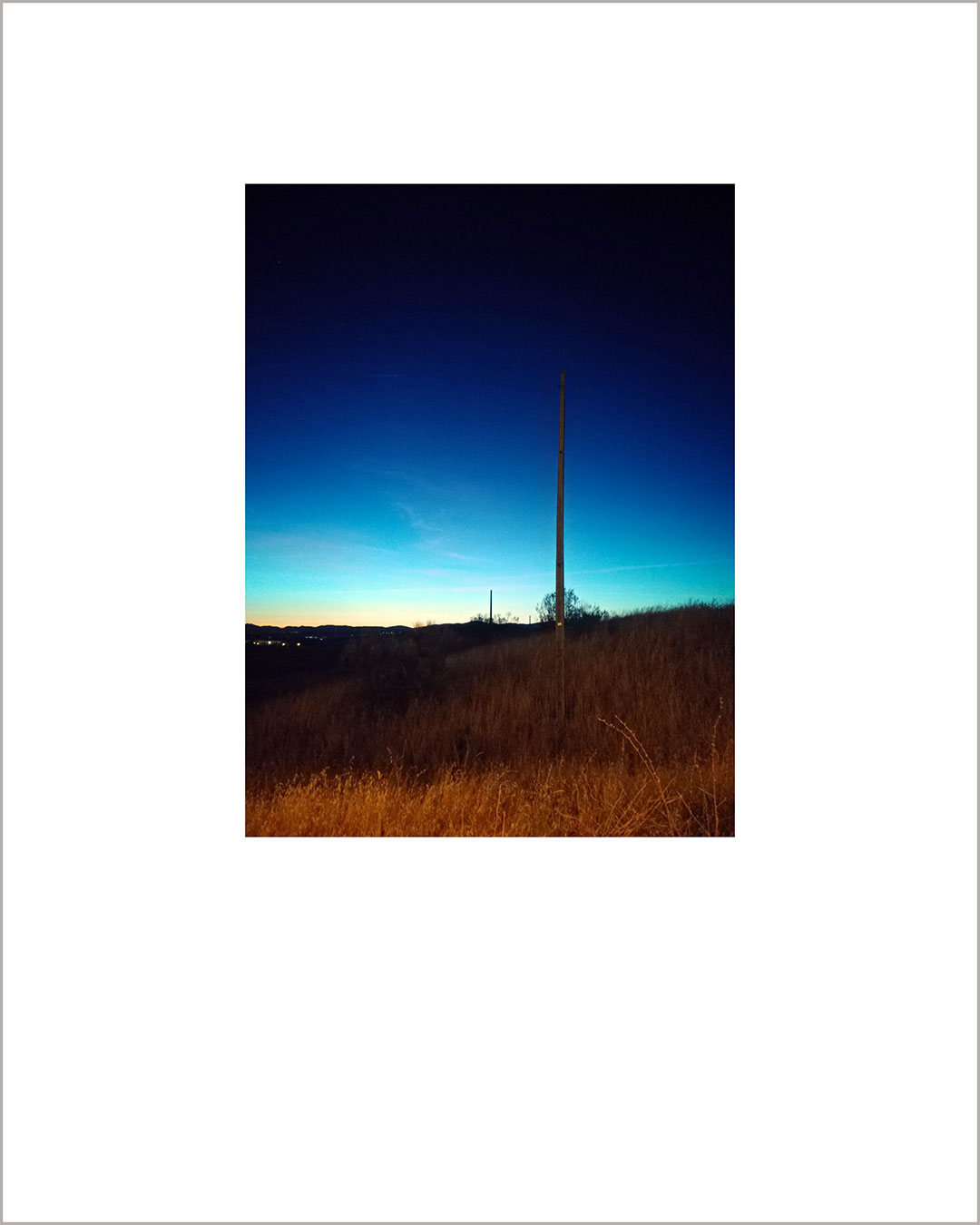 Fotografía vertical de un anochecer, en el suelo hay paja naranja y el cielo se funde del azul al negro