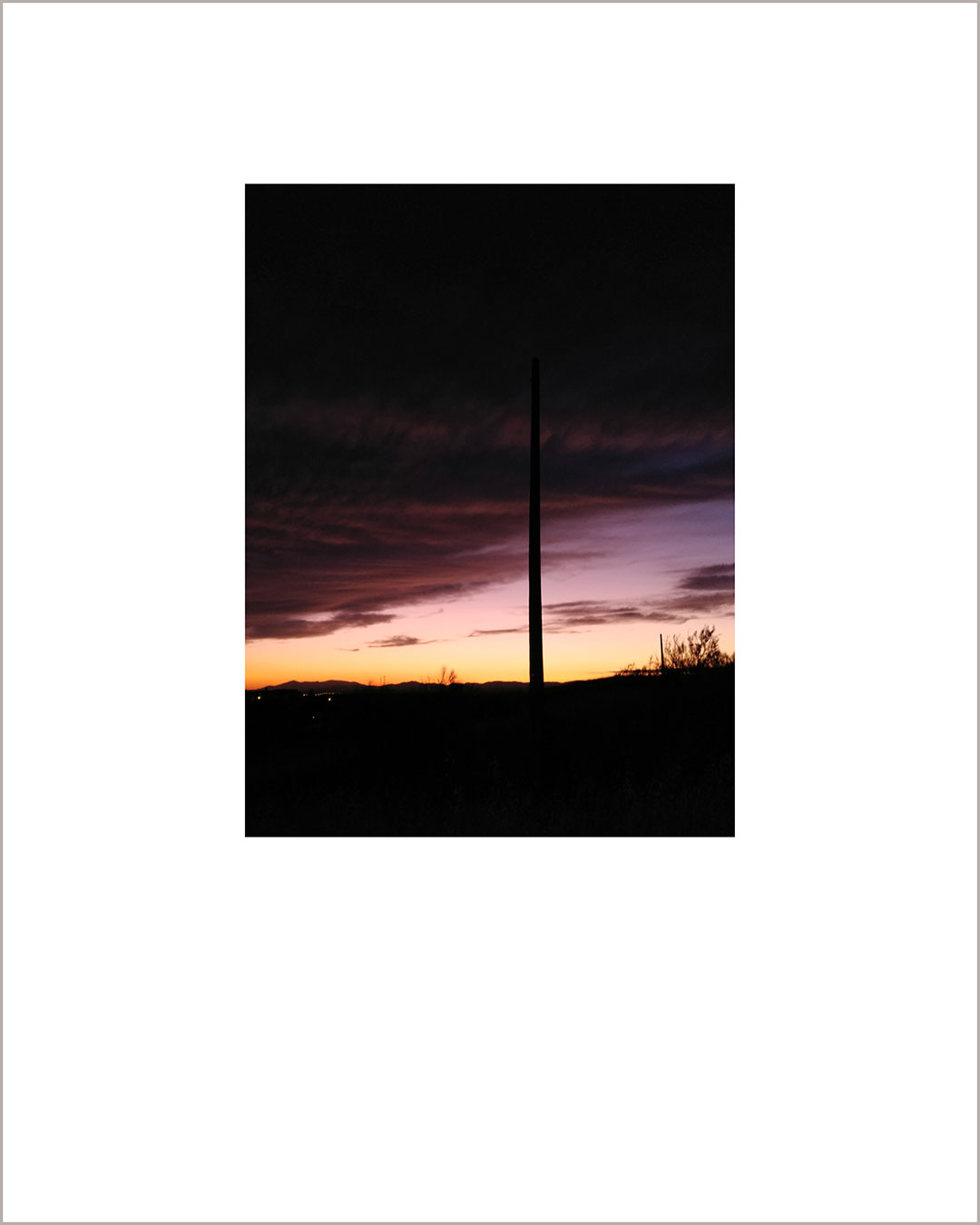Fotografía vertical de un anochecer, suelo negro y cielo en tonos amarillos y con grandes nubes granates.
