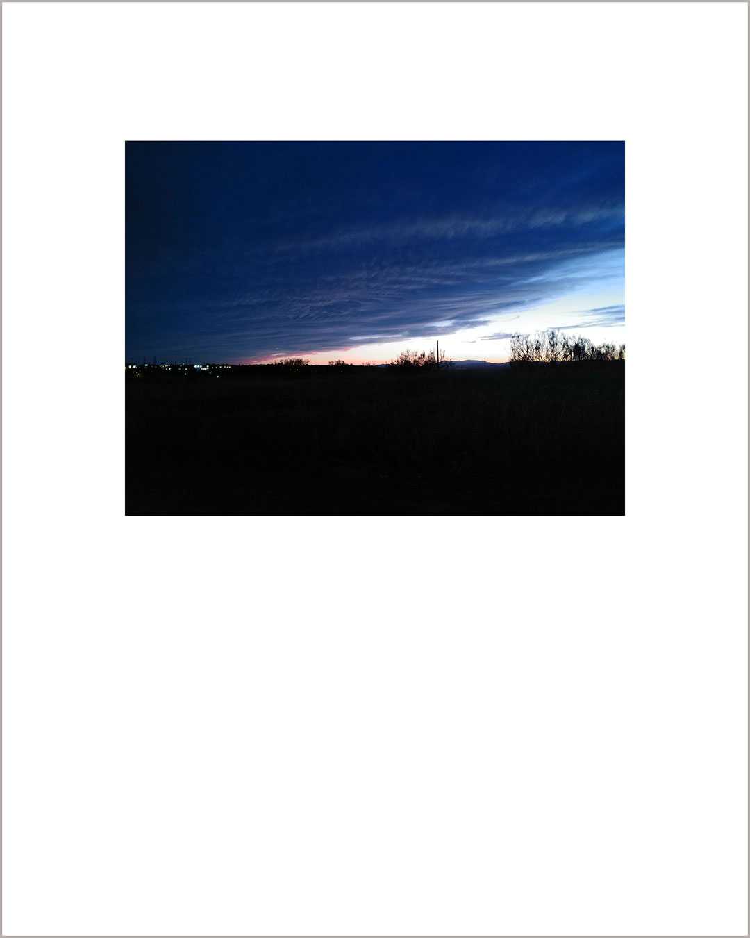 Fotografía horizontal de un atardecer, el suelo es negro y el cielo está cubierto de nubes color añil.