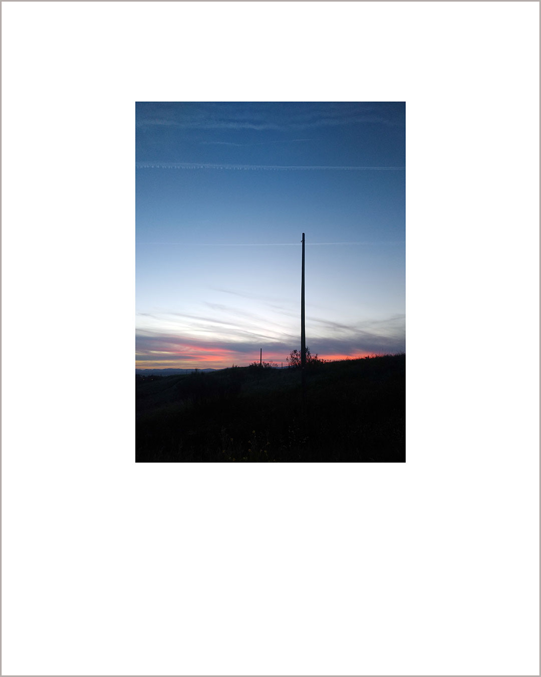Fotografía vertical de un atardecer, suelo negro con la silueta de un poste y cielo añil.