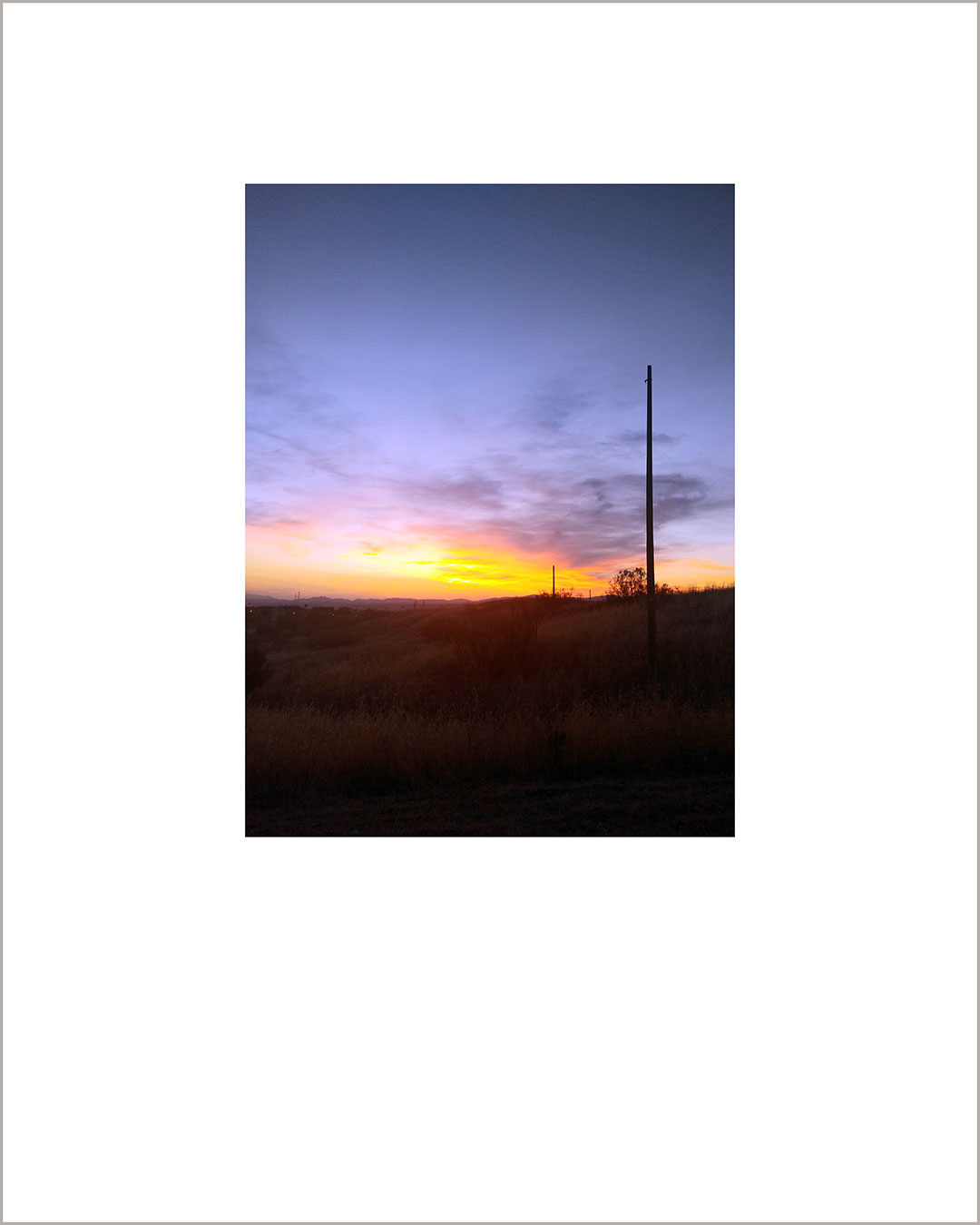Fotografía vertical de un atardecer, con el suelo negro y el cielo amarillo y violeta.