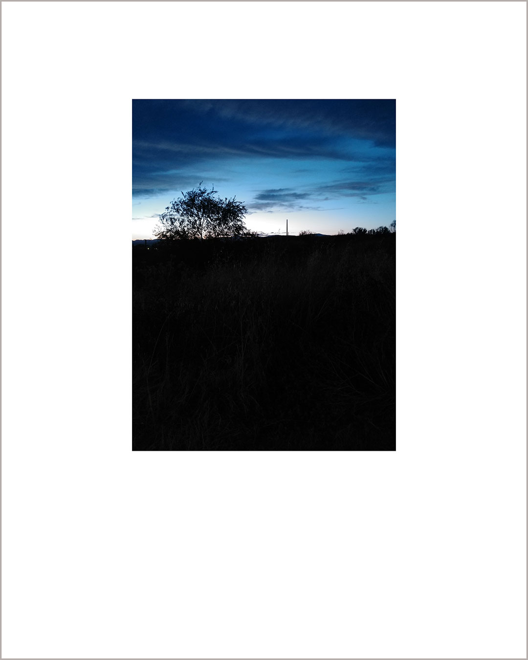 Fotografía vertical de un anochecer, los dos tercios inferiores los ocupa un suelo negro, que queda recortado sobre el cielo azul oscuro.