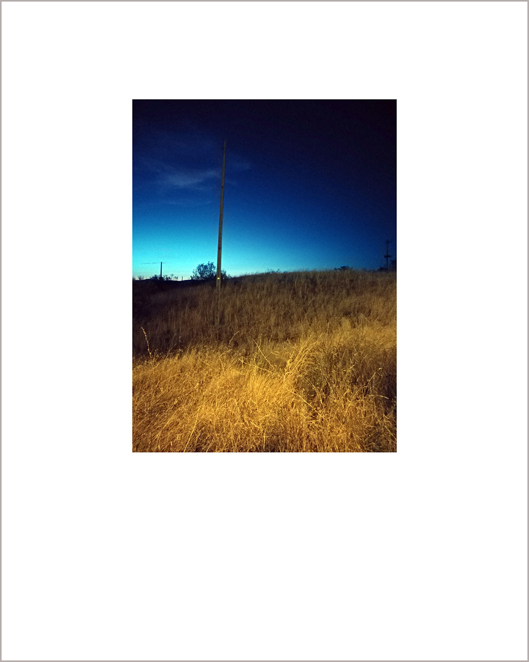 Fotografía vertical de un anochecer, en el suelo hay paja amarilla y el cielo se funde del azul al negro.