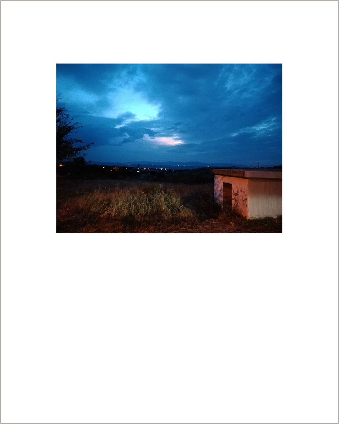 Fotografía horizontal de un atardecer, a la derecha se ve una caseta, el cielo está cubierto de nubes color añil.